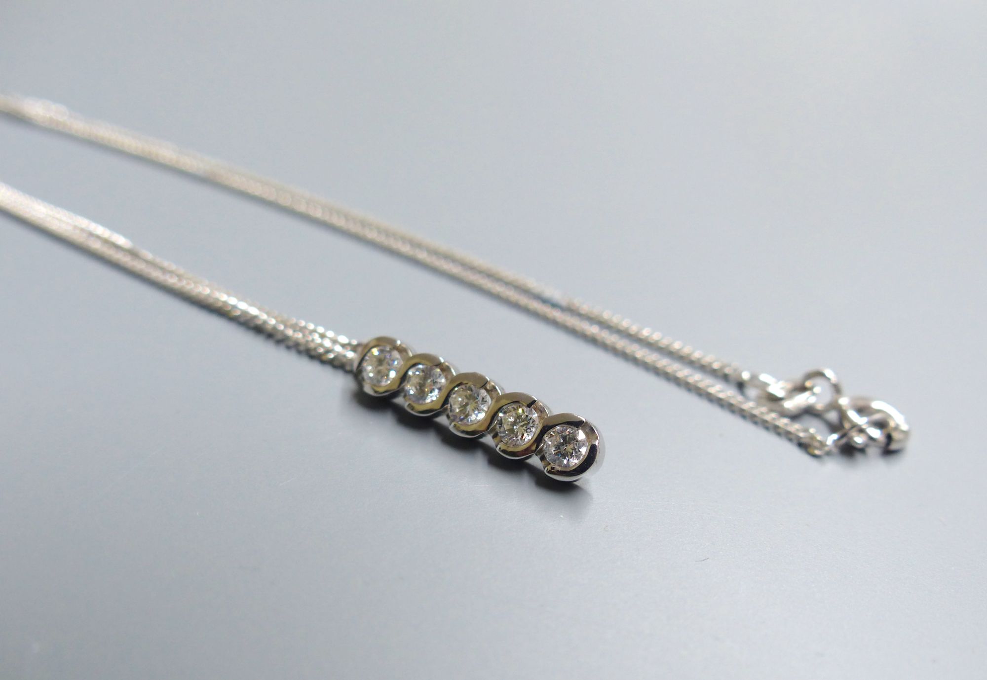 A modern 18ct white gold and five stone diamond set line pendant, on an 18ct white gold fine link chain,
